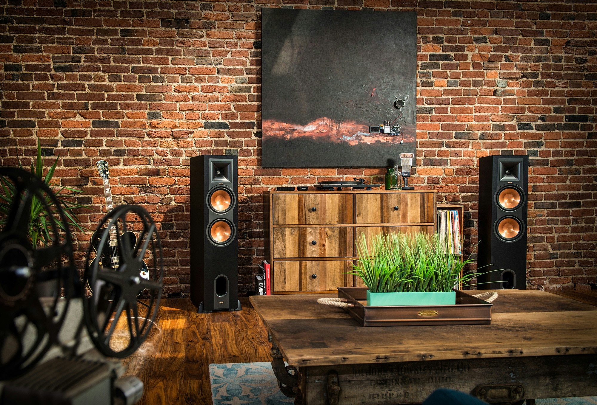 Two R-28PF powered floorstanding speakers flanking a painting and dresser